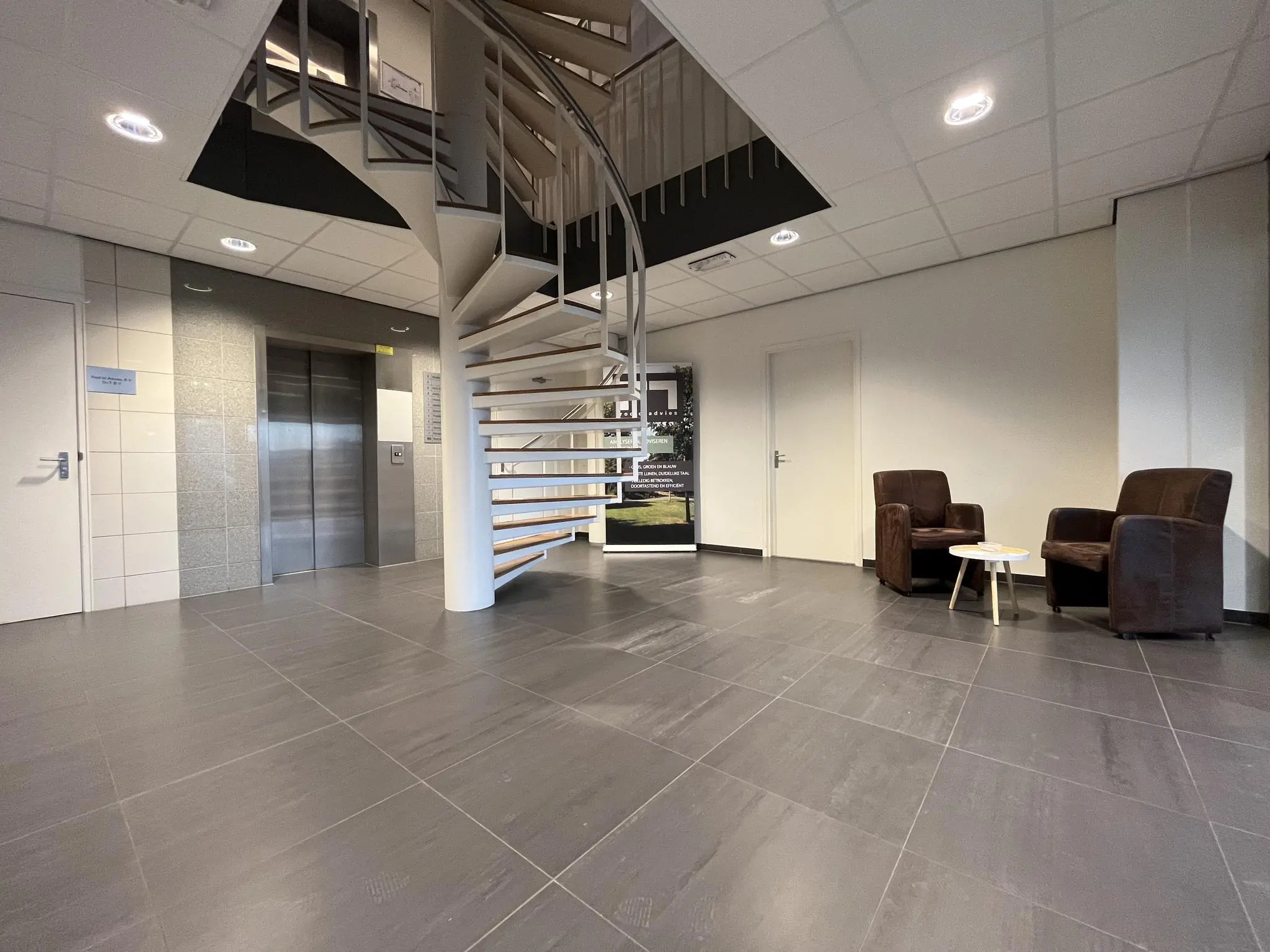Moderne ontvangstruimte in kantoorpand in Leidse Rijn met wenteltrap, lift en zitgedeelte.